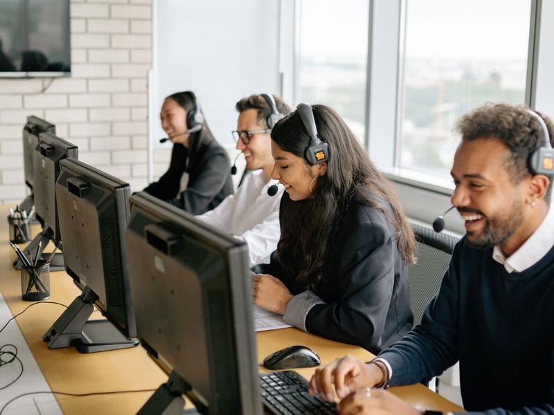 A smiling sales team with headsets at their desks